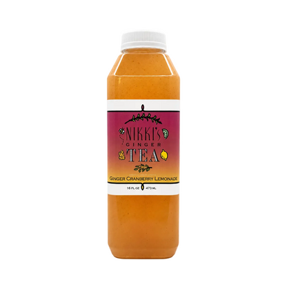 A bottle of Nikki's Ginger Tea in the Ginger Cranberry Lemonade flavor, filled with an orange-amber liquid, featuring a white cap and a magenta label, set against a plain off-white background.