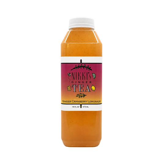 A bottle of Nikki's Ginger Tea in the Ginger Cranberry Lemonade flavor, filled with an orange-amber liquid, featuring a white cap and a magenta label, set against a plain off-white background.