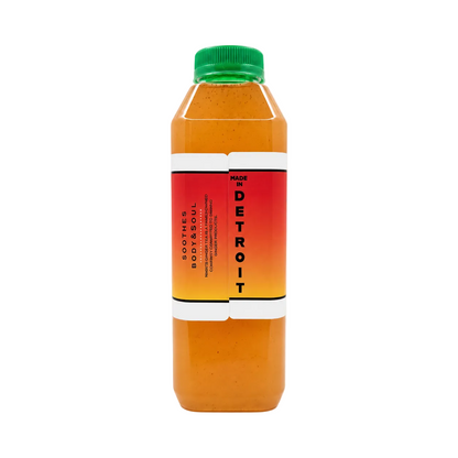 A bottle of amber colored lemonade, featuring an orange and red gradient label with a green cap, set against a plain off-white background.